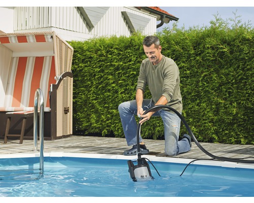 Ein Mann bedient eine Tauchpumpe zur Entleerung eines Pools im Garten.