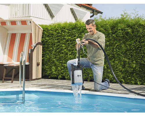 Mann benutzt eine Tauchpumpe am Pool zur Wasserentleerung.