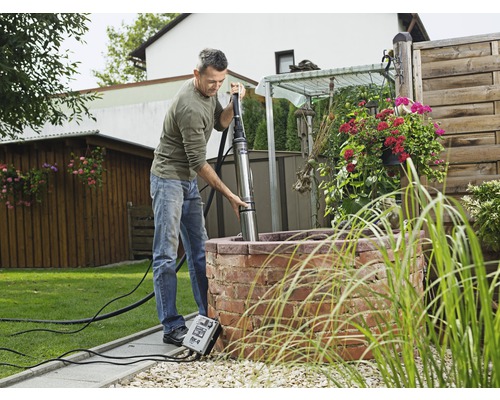 Ein Mann installiert eine Tiefbrunnenpumpe in einem Gartenbrunnen.