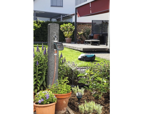 Gartenszene mit Wasserhahn, Bewässerungssteuerung und Rasenmähroboter im Garten