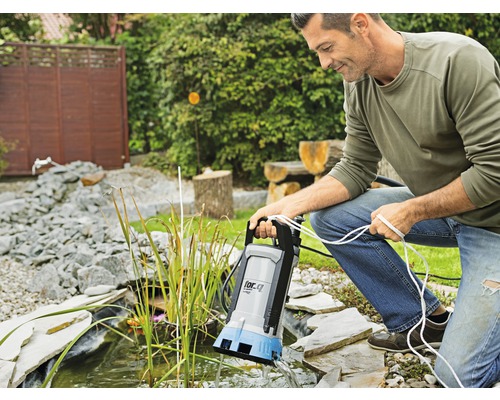 Mann bedient eine Teichpumpe am Gartenteich.