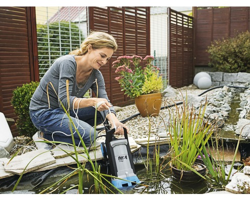 Frau bedient eine Teichpumpe der Marke for_q in einem Gartenteich.