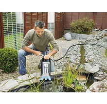 Ein Mann bedient eine Teichpumpe am Rande eines Gartenteichs der mit Steinen umrandet ist.