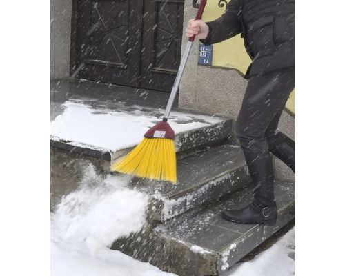 Eine Person kehrt Schnee mit einem Besen von einer Treppe.