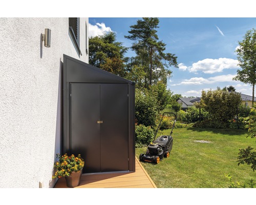 Geräteschuppen aus Metall im Garten neben einem Rasenmäher.