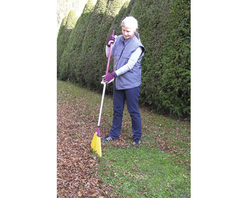 Eine Frau kehrt Laub mit einem Straßenbesen im Garten.