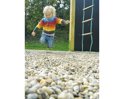 Ein Kind springt auf einem Spielplatz neben einer Kletterwand und einer Strickleiter.