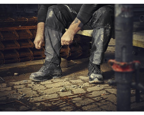Ein Bauarbeiter sitzt und bindet seine Arbeitsschuhe auf einer Baustelle.