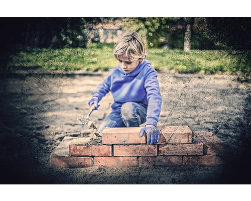 Junge baut eine Ziegelmauer mit einer Maurerkelle im Garten