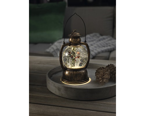 Dekorative Schneekugellaterne mit Schneemann und Weihnachtsbaum auf einem Tablett