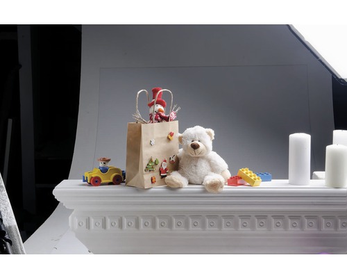 Dekorative Szene mit Geschenk, Teddybär, Spielzeug und Kerzen auf einem Kaminsims