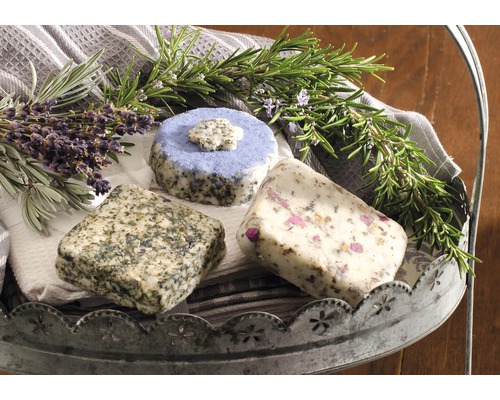 Drei Kräuterseifen mit Lavendel, Rosmarin und Rosenblüten auf einer Servierplatte
