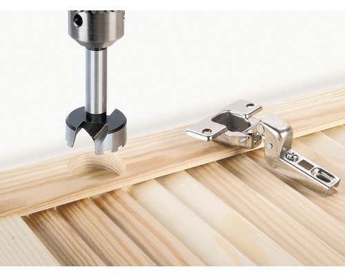 Forstnerbohrer bohrt Loch neben einem Topfband in eine Holzplatte.