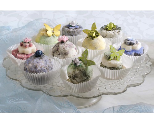 Dekorative Seifenstücke in Papierförmchen mit Schmetterlingen und Blumen auf einem Glasteller