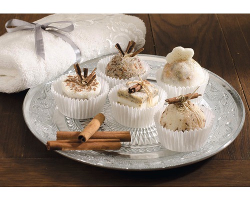 Dekorative Seifenstücke in Muffinförmchen mit Zimtstangen auf einem silbernen Teller, zusammen mit einem Handtuch.