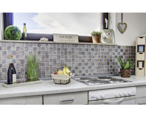 Küchenszene mit Mosaikfliesen, Kochfeld, Dekorationen und Lebensmitteln auf einer Küchentheke.