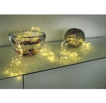 Dekorative Lichterkette drapiert um eine Glasschale und eine Kugelvase auf einem Möbelstück.
