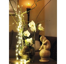 Dekorative Glasvase mit Orchideenblüten, Zweigen und Lichterkette neben einer Engelstatue