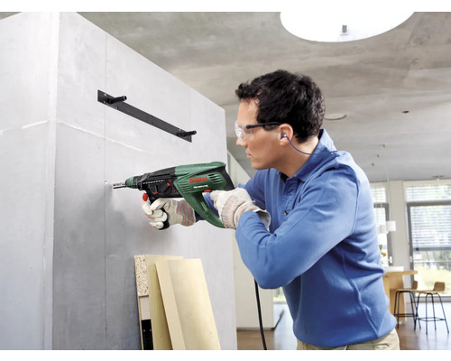 Mann bohrt mit einer Schlagbohrmaschine in eine Wand, um eine Halterung anzubringen