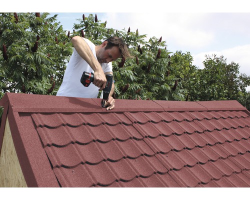 Mann montiert Dach eines Gartenhauses mit Akkuschrauber