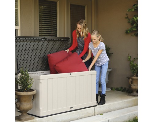 Mutter und Tochter verstauen Kissen in einer Gartenbox aus Kunststoff.