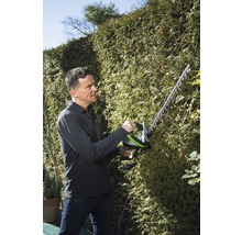 Mann schneidet Hecke mit einer Heckenschere.