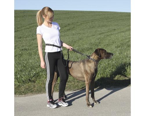 Frau führt Hund an einer Hüftleine im Freien aus