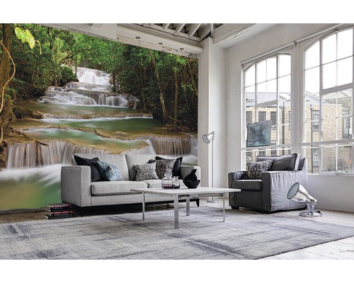Wohnzimmer mit Fototapete eines Wasserfalls in einem Wald, hellem Sofa, Sessel und Teppich.