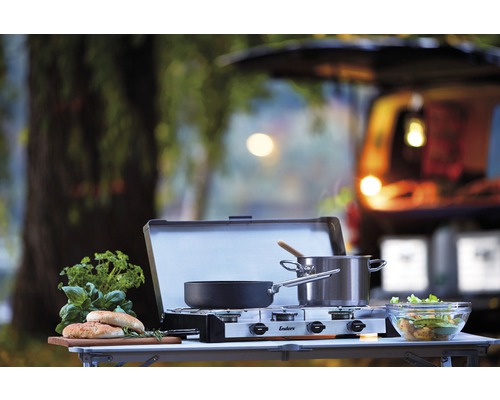 Campingküche mit Gaskocher, Töpfen, Zutaten und einem Auto im Hintergrund für Outdoor-Kocherlebnisse