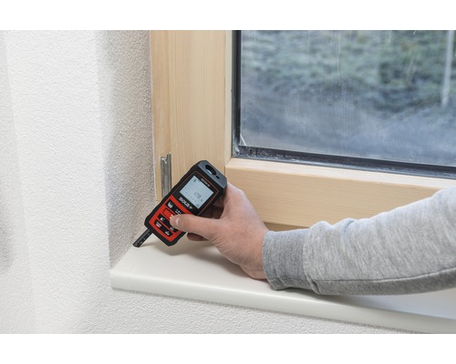 Eine Person misst mit einem Laser-Entfernungsmesser einen Fensterrahmen.