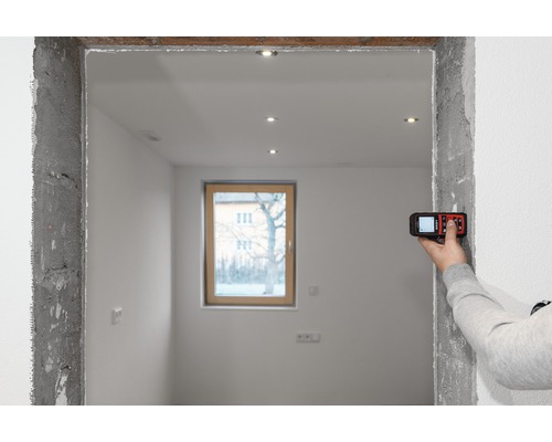 Ein Raum im Rohbau mit einer Person, die mit einem Laser-Entfernungsmesser eine Messung an einem Türrahmen durchführt.