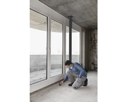 Handwerker misst mit einem Laser-Entfernungsmesser die Länge eines Fensters in einem Rohbau.