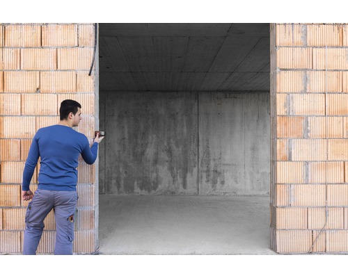 Mann benutzt Wasserwaage an Ziegelwand im Rohbau