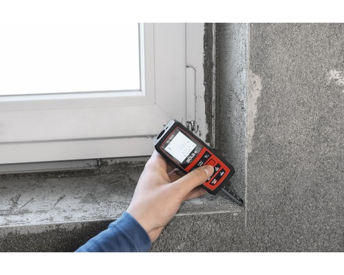 Hand misst mit Laser-Entfernungsmesser Abstand an Fenster