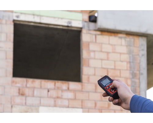 Person hält ein Feuchtigkeitsmessgerät vor einer Ziegelwand