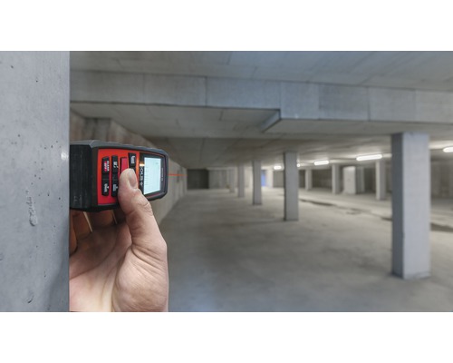 Eine Person misst mit einem Laser-Entfernungsmesser den Abstand in einer Tiefgarage.