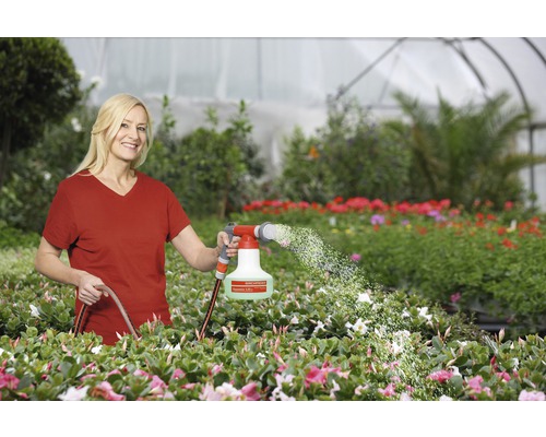 Frau bewässert Pflanzen mit einer Gartenspritze in einem Gewächshaus.
