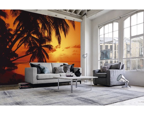 Wohnraum mit Fototapete mit Palmenmotiv und Sonnenuntergang am Strand, Sofa, Sessel, Teppich und Couchtisch