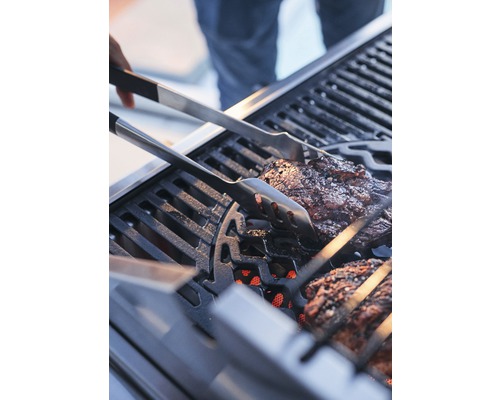Fleisch wird mit einer Grillzange auf einem Grill gewendet.