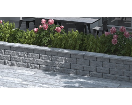Mauer aus Betonsteinen mit Pflanzen und Blumen im Außenbereich.