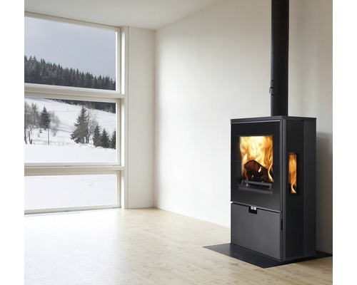 Innenaufnahme eines Raumes mit einem schwarzen Kaminofen und einem Fenster mit Blick auf eine verschneite Landschaft