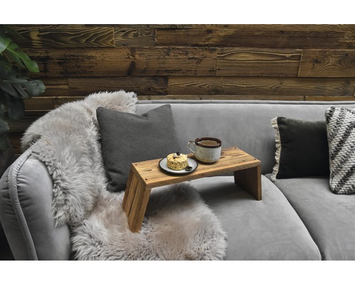 Graues Sofa mit Kissen, Fell und Serviertablett mit Tasse und Kuchen vor einer Holzwand