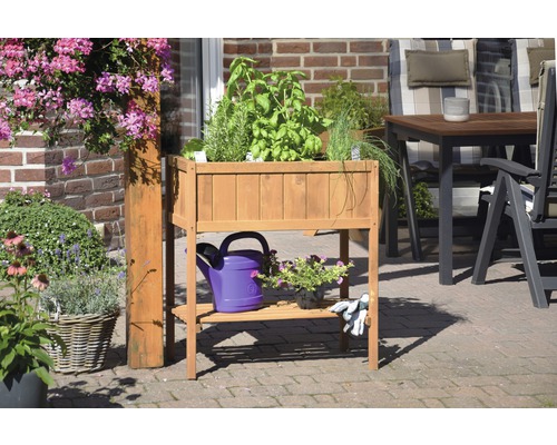 Hochbeet aus Holz mit Kräutern, Gießkanne und Gartenhandschuhen auf einer Terrasse