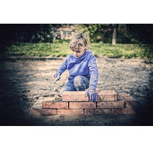 Junge baut eine Mauer mit Steinen und einer Maurerkelle