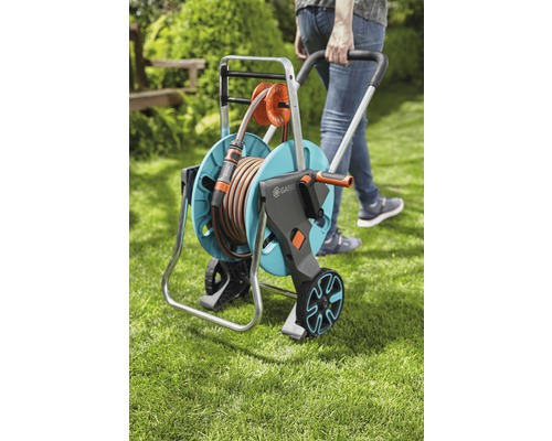 Person zieht einen Gartenschlauchwagen mit einem Schlauch darauf durch den Garten.