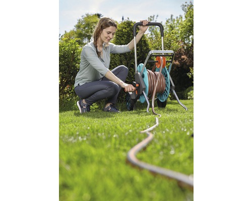 Frau bedient Schlauchwagen im Garten mit Gartenschlauch