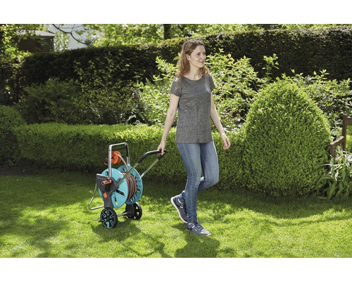 Frau zieht einen Gartenschlauchwagen auf einer Rasenfläche.