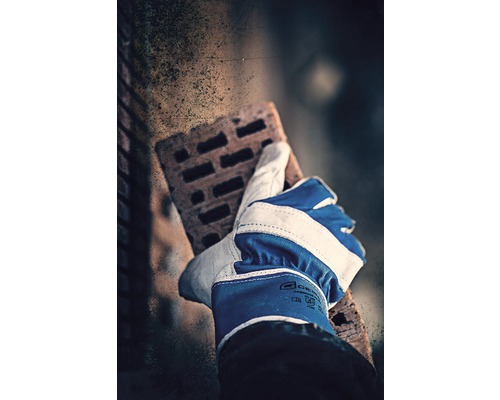 Eine Hand mit einem Arbeitshandschuh hält einen Mauerziegel.