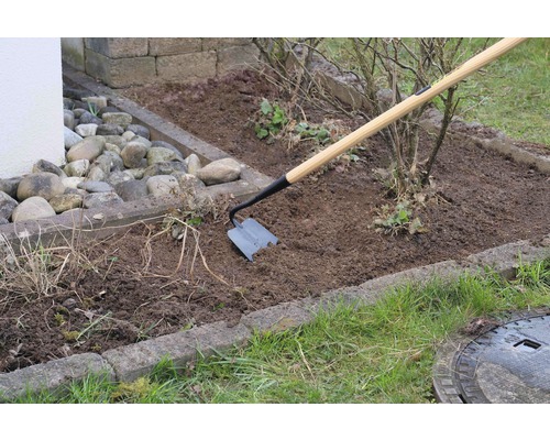 Gartenharke mit Holzstiel im Einsatz in einem Gartenbeet