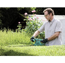 Mann schneidet Hecke mit einer Heckenschere im Garten